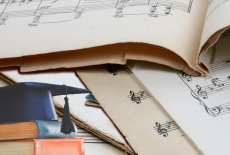 Sheet music and a stack of books with a graduation cap on top.