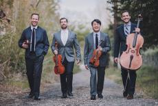 The Miro Quartet walking together down a gravel path with greenery on both sides.