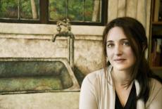 headshot of Simone Dinnerstein in an off white sweater in front of a painting of a kitchen