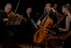 violin, cello, viola, and piano in performance together against a black background