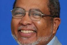 Adolphus Hailstork headshot, he is smiling, wearing thin rimmed glasses, and in front of a blue background