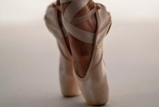 A close up of a ballerina's feet en pointe, wearing cream colored pointe shoes.