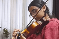 Lubna Alyaan is playing her violin and wearing a red sweater.
