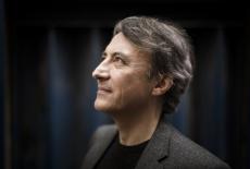 A side profile picture of pianist Bavouzet, wearing a black shirt and light black sportcoat