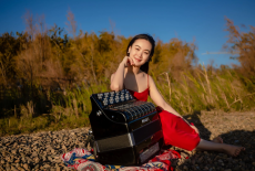 Hanzhi in a red dress posing outside on a rocky surface with her accordion