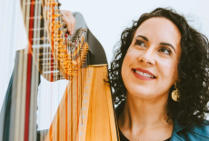 Close up of Nadia's face next to her harp, we see strings, the golden wood color, as she looks upwards.