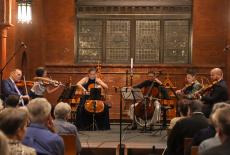 a sextet of string players perform in a church, with a mostly brick background.