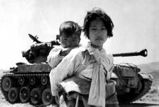 A Korean girl trudges by a stalled M-26 tank with her brother on her back