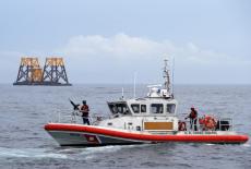 U.S. Coast Guard patrol boat passes a barge carrying jacket supports and platforms for wind turbines in the waters of the ...