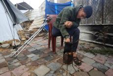 Displaced Palestinian Mahmoud Abu al-Kas, who has an amputated leg, sits tending a small fire in front of his family's mak...
