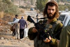 Israeli soldiers check the identity cards of Palestinians entering their land to harvest olives during the annual olive-pi...