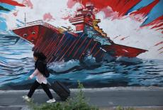 An Iranian woman walks next to a mural on a street in Tehran