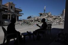 A couple returning to their village after being displaced by the war, sits in front of a house belonging to their neighbou...