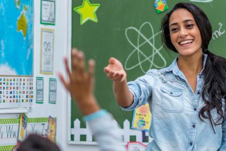 A teacher stands in front of raised hands in the classroom.