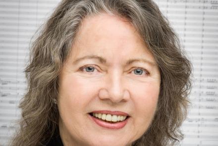 A headshot of the composer Ellen Taafe Zwilich with sheet music as the backdrop
