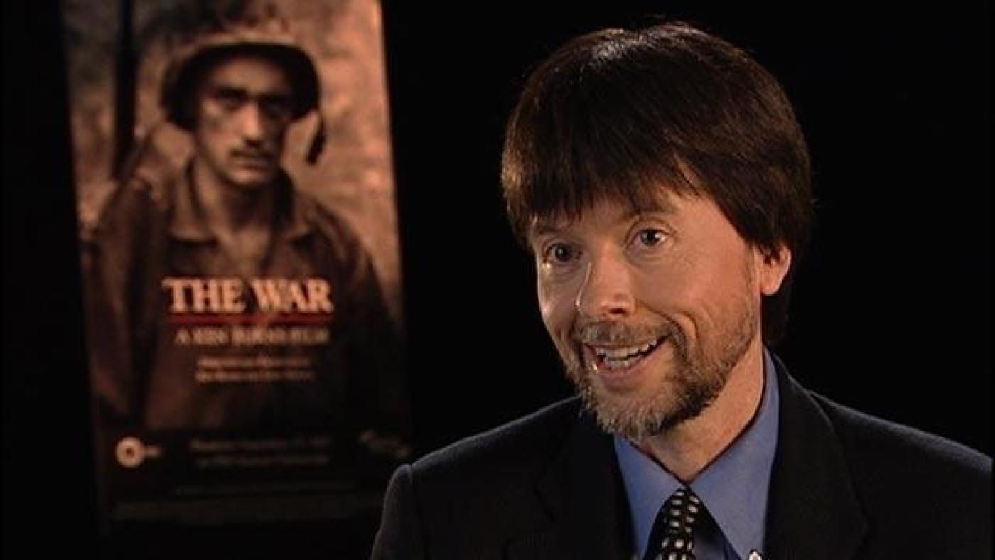 Ken Burns in front of a poster for his production, The War