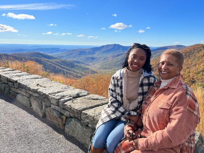 A young woman and her mother sit on a rock bench with Virginia mountains in the background