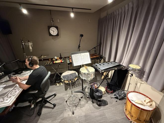 Chris sitting at a table with over a dozen percussion instruments behind him