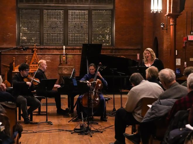A mid performance picture featuring Chiarina as a piano trio with soprano, dark brick background